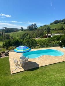 a swimming pool with an umbrella and two chairs and a table and an umbrella at Casa no Vale dos Vinhedos em Bento Gonçalves in Bento Gonçalves
