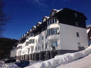 un grande edificio bianco con un tetto nero nella neve di Apartments Monika a Špindlerův Mlýn