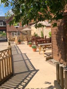 eine Terrasse mit Holzbänken, Tischen und einem Baum in der Unterkunft The Boot and Shoe Inn in Flintham