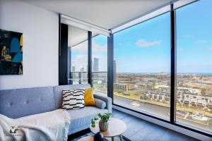 sala de estar con sofá azul y ventanas grandes en KOZYGURU DOCKLANDS LUXURY WATER VIEW APT 1 BED VDO915, en Melbourne
