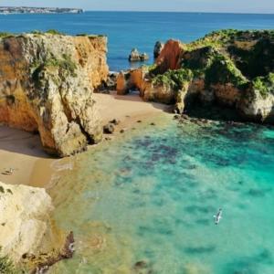 a beach with rocks and water and a person in the water at APARTAMENTO COR DO MAR - Sunny, Clean and spacious apartment with sea view, in Alvor - very close walking distance to the beach and Alvor Village in Alvor