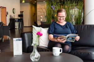 une femme assise sur un canapé qui lit un livre dans l'établissement Cabinn Aalborg, à Aalborg