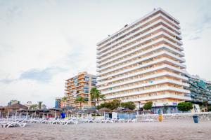 un grande edificio sulla spiaggia con sedie e ombrelloni di Apartamentos Stella Maris - Marcari SL a Fuengirola