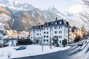 ein großes weißes Gebäude in einer verschneiten Straße mit Bergen in der Unterkunft Le Paradis 25 Apartment - Chamonix All Year in Chamonix-Mont-Blanc