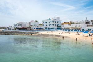 a beach with people on the sand and buildings at Calas Beach Corralejo in Corralejo