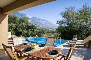 einen Holztisch und Stühle auf einer Terrasse mit einem Pool in der Unterkunft Villa Yianna in Karavádhos