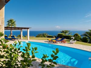 a swimming pool with two blue chairs and the ocean at Villa Dimitra in Trapezaki