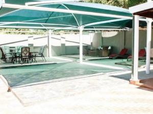 un patio con ombrellone, sedie e tavoli verdi di Monacco Guest house a Bronkhorstspruit