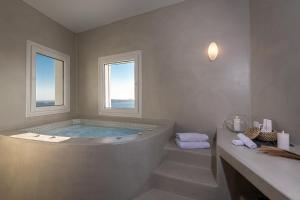 a bathroom with a large tub with two windows at Adamant Suites in Fira