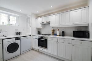 a white kitchen with white cabinets and a washer and dryer at Stylish Sloane Square Home Close to Victoria by UndertheDoormat in London
