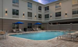 einem Pool vor einem Gebäude mit Stühlen und Sonnenschirmen in der Unterkunft Holiday Inn Express Jacksonville Beach, an IHG Hotel in Jacksonville Beach