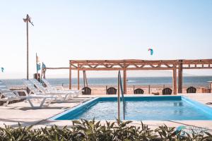 a swimming pool next to a beach with chairs and the ocean at Bamboo Paracas Resort in Paracas