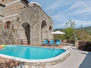 una piscina frente a un edificio de piedra con sillas y sombrilla en Flat with heated hot tub and shared pool, en Casola in Lunigiana
