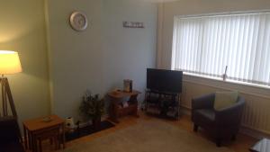 uma sala de estar com uma televisão, uma cadeira e uma janela em Delightful house with big ambitions em Leigh