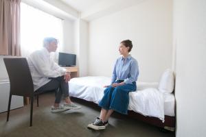 
a man and a woman sitting on a bed at Heiwadai Hotel Arato in Fukuoka
