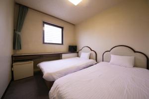 two beds in a room with white sheets and a window at Heiwadai Hotel Otemon in Fukuoka