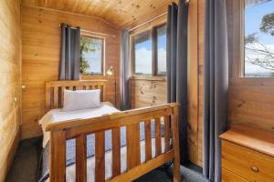Cabaña de madera con cama en habitación con ventanas en Mole Creek Cabins en Mole Creek
