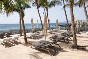 a group of lounge chairs and umbrellas on the beach at Hotel Fariones in Puerto del Carmen
