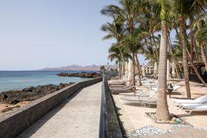 a beach with chairs and palm trees and the ocean at Hotel Fariones in Puerto del Carmen