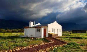 a small white house in a field with a storm at Duikersdrift Winelands Country Escape in Tulbagh