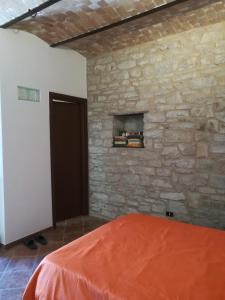 1 dormitorio con pared de piedra y 1 cama con sábanas de color naranja en Guado di Pio- monolocale en Il Guasto