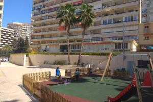 dwójka dzieci siedzących na placu zabaw przed budynkiem w obiekcie APARTAMENTO RINCÓN DE LOIX ( PLAYA DE LEVANTE) w mieście Benidorm