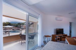a room with a balcony with a table and a television at Ilhabela Beach Residences in Ilhabela