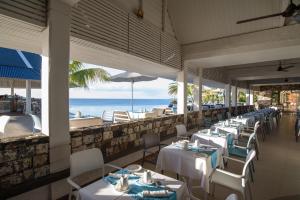 a restaurant with white tables and chairs and the ocean at Anelia Resort & Spa in Flic-en-Flac