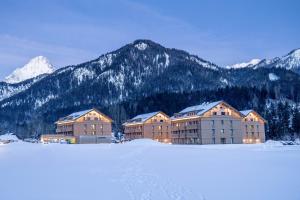 a building in the snow with mountains in the background at Dormio Aparthotel Hinterstoder in Hinterstoder