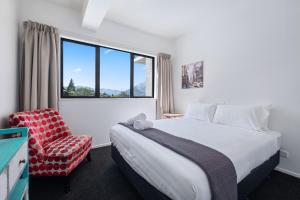 een slaapkamer met een bed, een stoel en een raam bij Brookside Gem - Modern 2 Bedroom Apartment in Queenstown