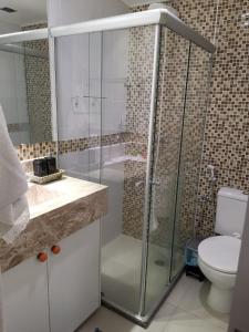 uma casa de banho com uma cabina de duche em vidro e um WC. em Village em Guarajuba