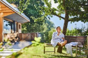 a woman sitting on a bench under a tree at ElzLand Hotel Pfauen WELLNESS & SPA in Elzach