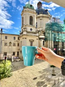 una mano che tiene una tazza blu di fronte a un edificio di Dreaming Apartments a Lviv