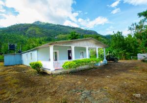 a small white house with mountains in the background at Moonlight Munnar Forest Bungalow with Private Waterfalls by VOYE HOMES in Kanthalloor