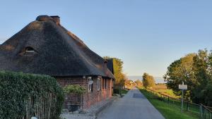 an old brick building with a thatched roof and a road at Reetdachhaus Moordeichperle in Nordstrand