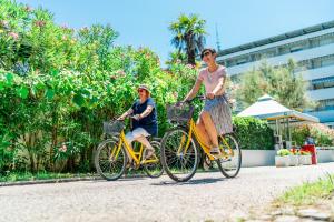 two people riding bikes down a street at Aparthotel Albatros in Lignano Sabbiadoro