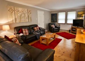 a living room with a leather couch and a table at Bonnie Banks Cottage in Balloch