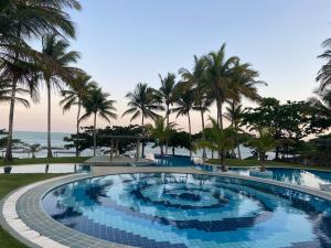 a swimming pool with palm trees and the ocean at Charmoso bangalô balinês pé na areia Outeiro das Brisas in Praia do Espelho