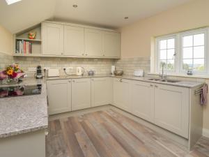 a kitchen with white cabinets and a wooden floor at Langham House Cottage in Lifton