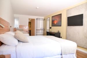 a bedroom with a large white bed and a flat screen tv at TAS D VIAJE Suites - Hostel Boutique in Punta del Este