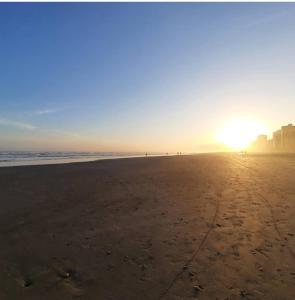 a beach with the sun setting on the horizon at O AP DO FÊ - Apartamento Praia Grande - Vila Tupi in Praia Grande
