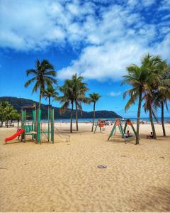 a group of playground equipment on a beach with palm trees at O AP DO FÊ - Apartamento Praia Grande - Vila Tupi in Praia Grande