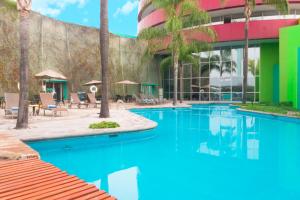 a swimming pool in front of a building with palm trees at Holiday Inn Monterrey-Parque Fundidora by IHG in Monterrey