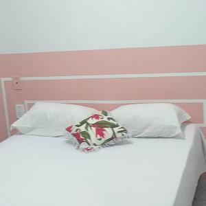 uma cama branca com 2 almofadas e uma cabeceira rosa em Pousada NOVA Catavento em Caraguatatuba