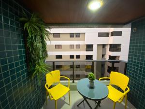 balkon z żółtymi krzesłami i stołem oraz budynek w obiekcie Apartamento na Ponta Verde Maceió Facilities w mieście Maceió