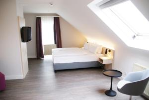 Schlafzimmer mit einem Bett, einem TV und einem Stuhl in der Unterkunft Taste Hotel Hockenheim in Hockenheim