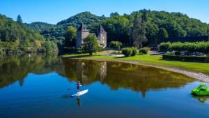 a man is standing on a paddle board in the water at Camping Le château du gibanel in Saint-Martial-Entraygues