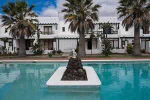 a swimming pool with a fountain in front of a building at Casa Neem - Duplex 2ch dans village naturiste in Charco del Palo