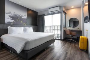 a bedroom with a bed and a desk with a yellow suitcase at Sleep Mai Chiang Mai Airport Lifestyle Hotel - SHA Plus in Chiang Mai