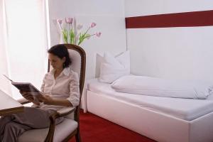 a woman sitting in a chair reading a book next to a bed at Arthotel Restaurant Pfeffermühle in Ingolstadt